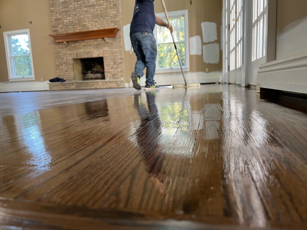 A professional technician from Precision Hardwood Flooring applying a final high-gloss topcoat to custom-stained dark hardwood floors in a Bergen County, NJ home.