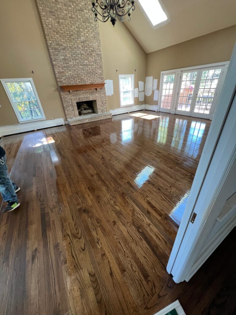 A wide-angle view of a luxury living room in Bergen County, NJ, showing professionally refinished oak hardwood floors with a rich dark stain and a reflective high-gloss protective coating.