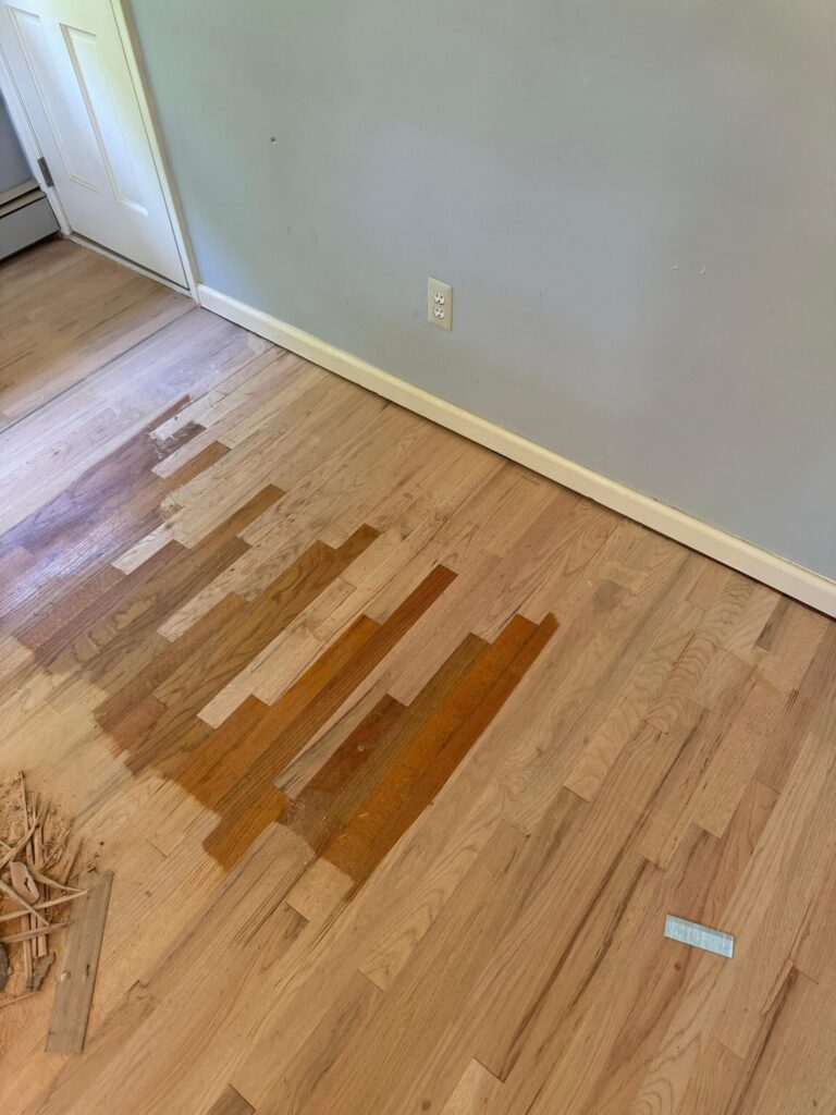 Precision Hardwood Flooring performing a weave-in repair on an oak floor in Bergen County, NJ, featuring multiple stain samples to ensure a perfect color match.