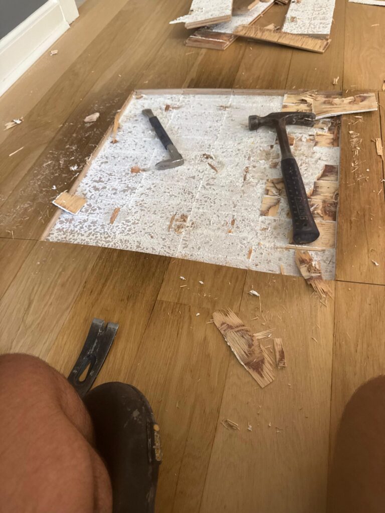 Precision Hardwood Flooring removing damaged oak planks from a residential floor in Bergen County, NJ, using a hammer and pry bar to prepare for a seamless repair.