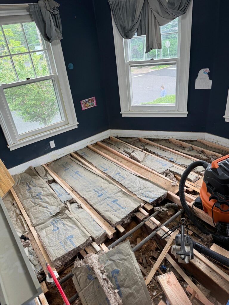 Bergen County home undergoing subfloor restoration by Precision Hardwood Flooring, showing exposed floor joists and professional debris removal in a room with dark blue walls.