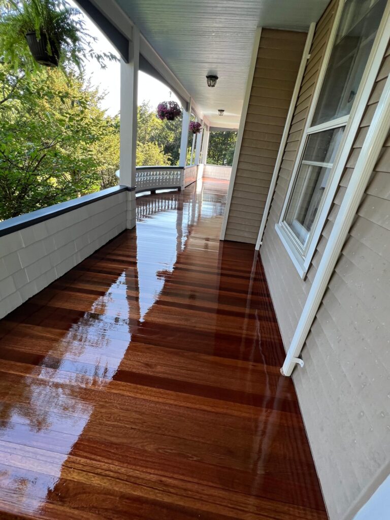 A long, elegant wraparound porch in Bergen County, NJ, featuring mahogany-toned wood planks with a mirror-like high-gloss finish by Precision Hardwood Flooring.