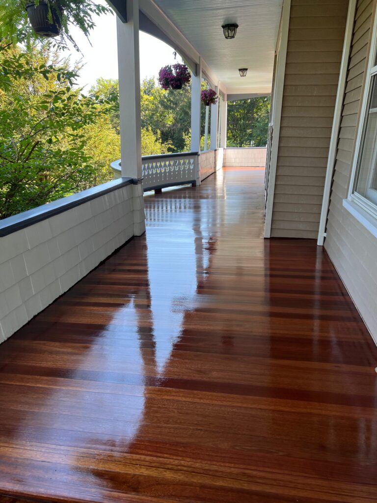 A wide wraparound porch in Bergen County, NJ, featuring mahogany-toned wood planks with a mirror-like high-gloss finish by Precision Hardwood Flooring.