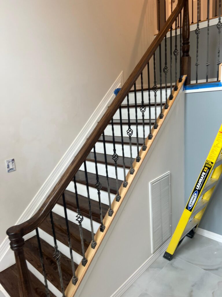 A refinished oak staircase by Precision Hardwood Flooring in Bergen County, NJ, featuring dark-stained treads, white risers, and decorative wrought iron spindles.