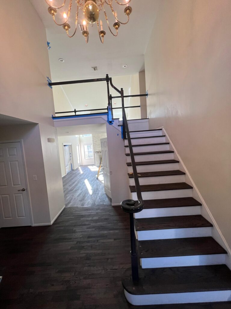 A luxury foyer in Bergen County, NJ, featuring a refinished oak staircase with dark espresso treads, white risers, and a matching custom handrail by Precision Hardwood Flooring.