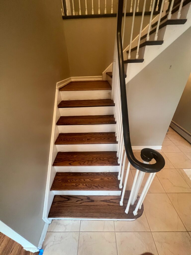A beautifully refinished hardwood staircase by Precision Hardwood Flooring in Bergen County, NJ, featuring dark stained wood treads, white risers, and a matching dark curved handrail.