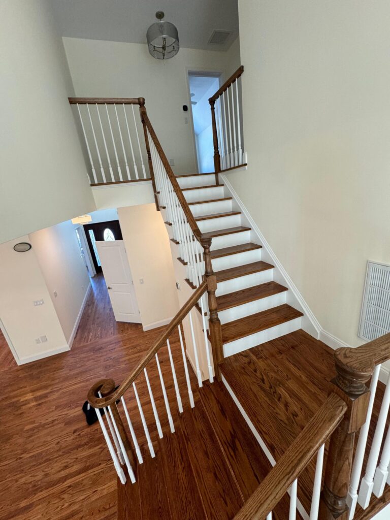 High-angle view of a professional hardwood staircase refinishing project by Precision Hardwood Flooring featuring oak treads and matching hallway flooring.