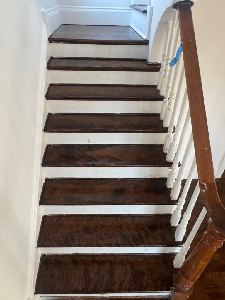A high-ceiling foyer in Bergen County, NJ, featuring wide-plank dark hardwood floors and a matching staircase with white risers by Precision Hardwood Flooring.
