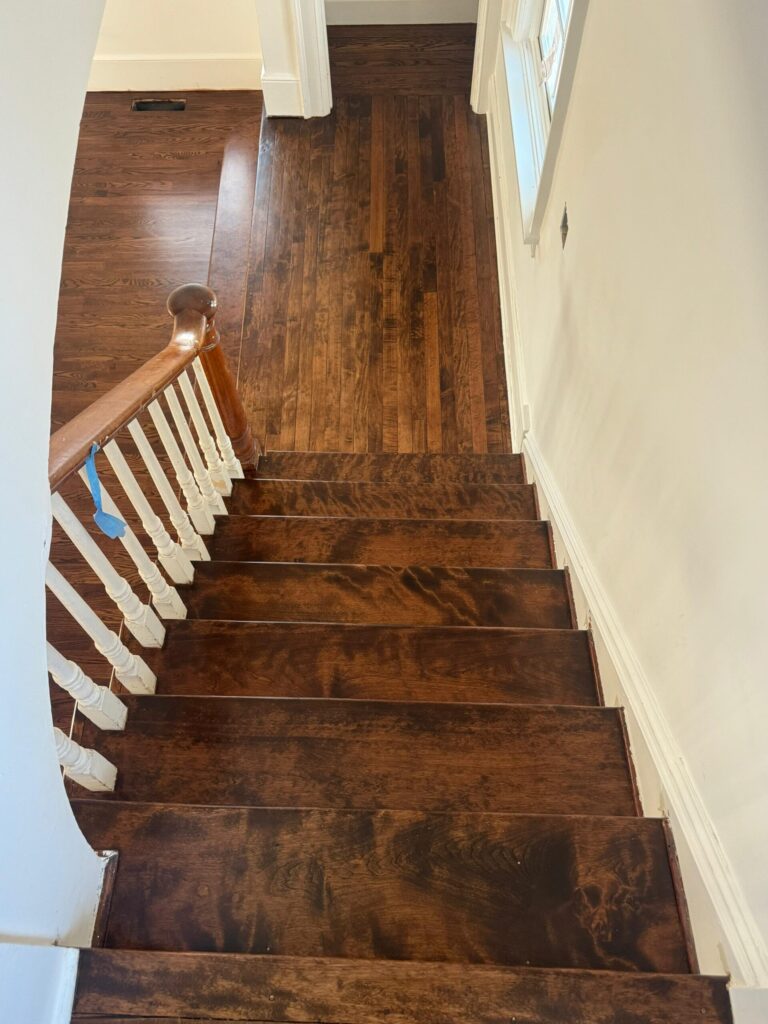 A high-angle view of a warm honey-toned oak hardwood floor and matching staircase with white balusters installed by Precision Hardwood Flooring in a Bergen County, NJ home.