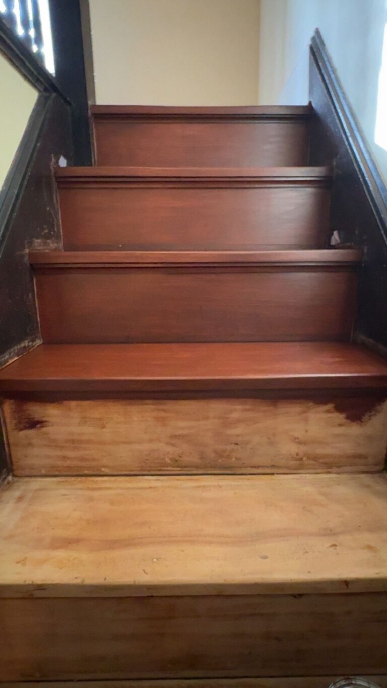A close-up view of a wooden staircase being refinished by Precision Hardwood Flooring in Bergen County, NJ, showing the transition from raw wood to a rich mahogany stain.