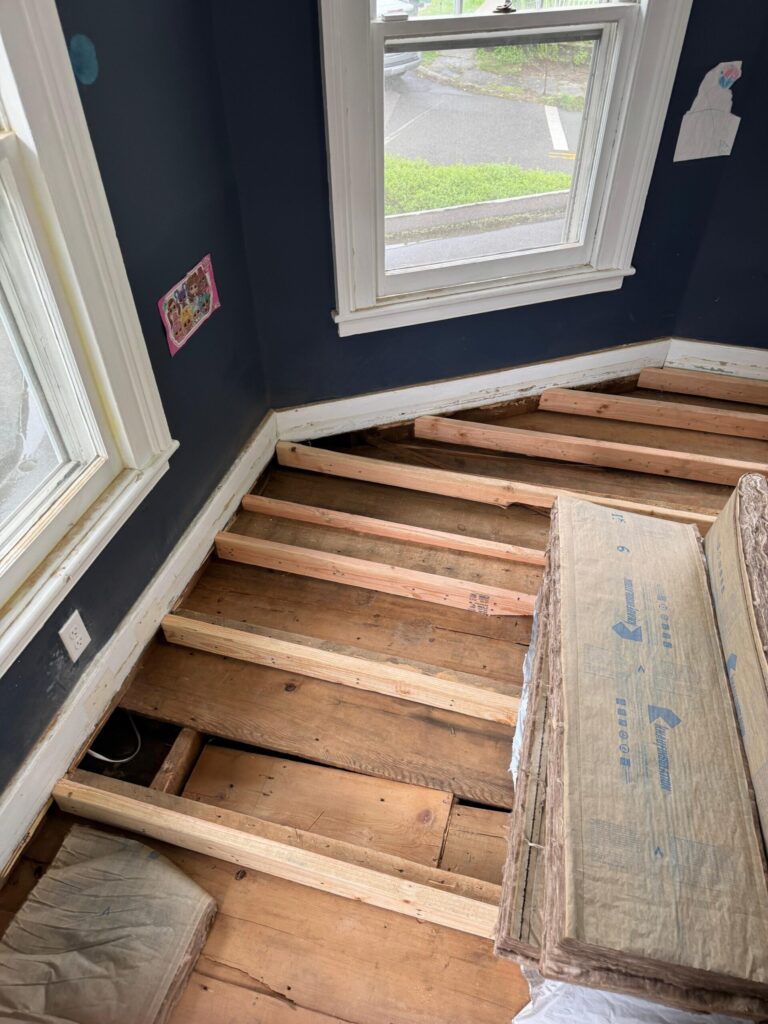 Floor renovation in progress with exposed wooden joists and subfloor inside a residential room, prepared for hardwood installation by Precision Hardwood Flooring.