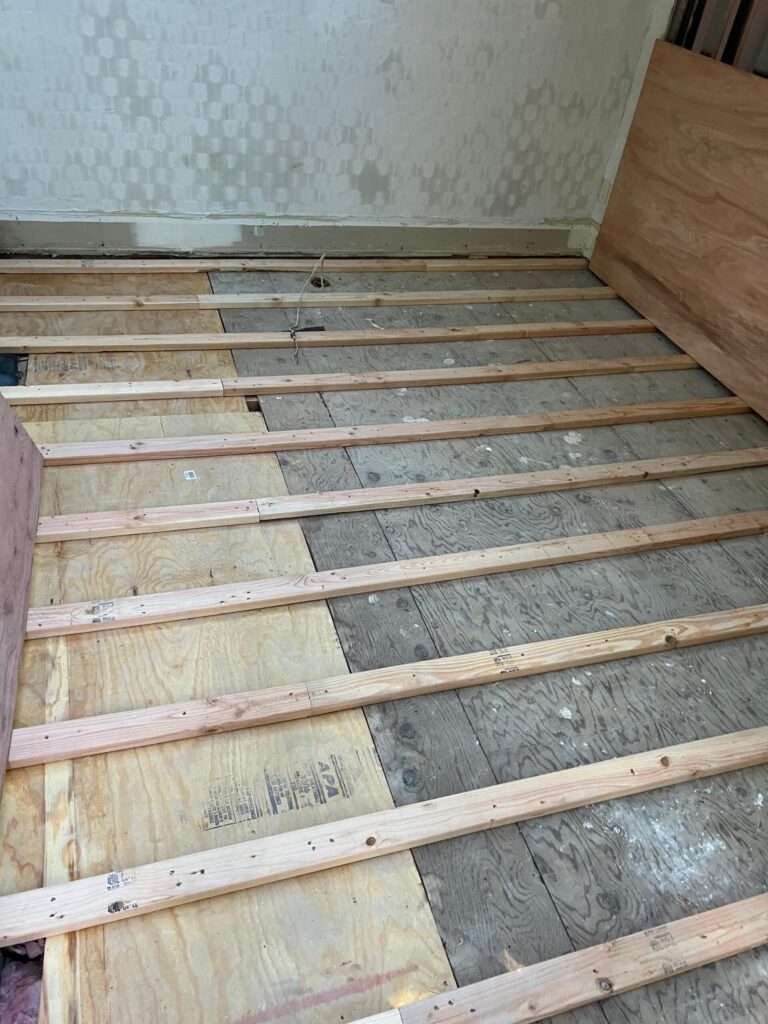 Precision Hardwood Flooring team preparing a plywood subfloor with wooden sleepers for a level hardwood floor installation in a Bergen County, NJ home.