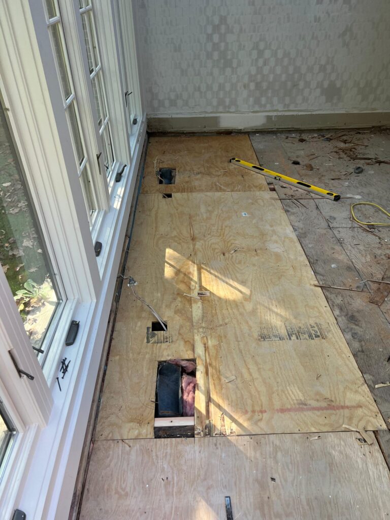 Precision Hardwood Flooring installing new plywood subfloor sheets near a large window in a Bergen County, NJ home to create a stable base for hardwood installation.